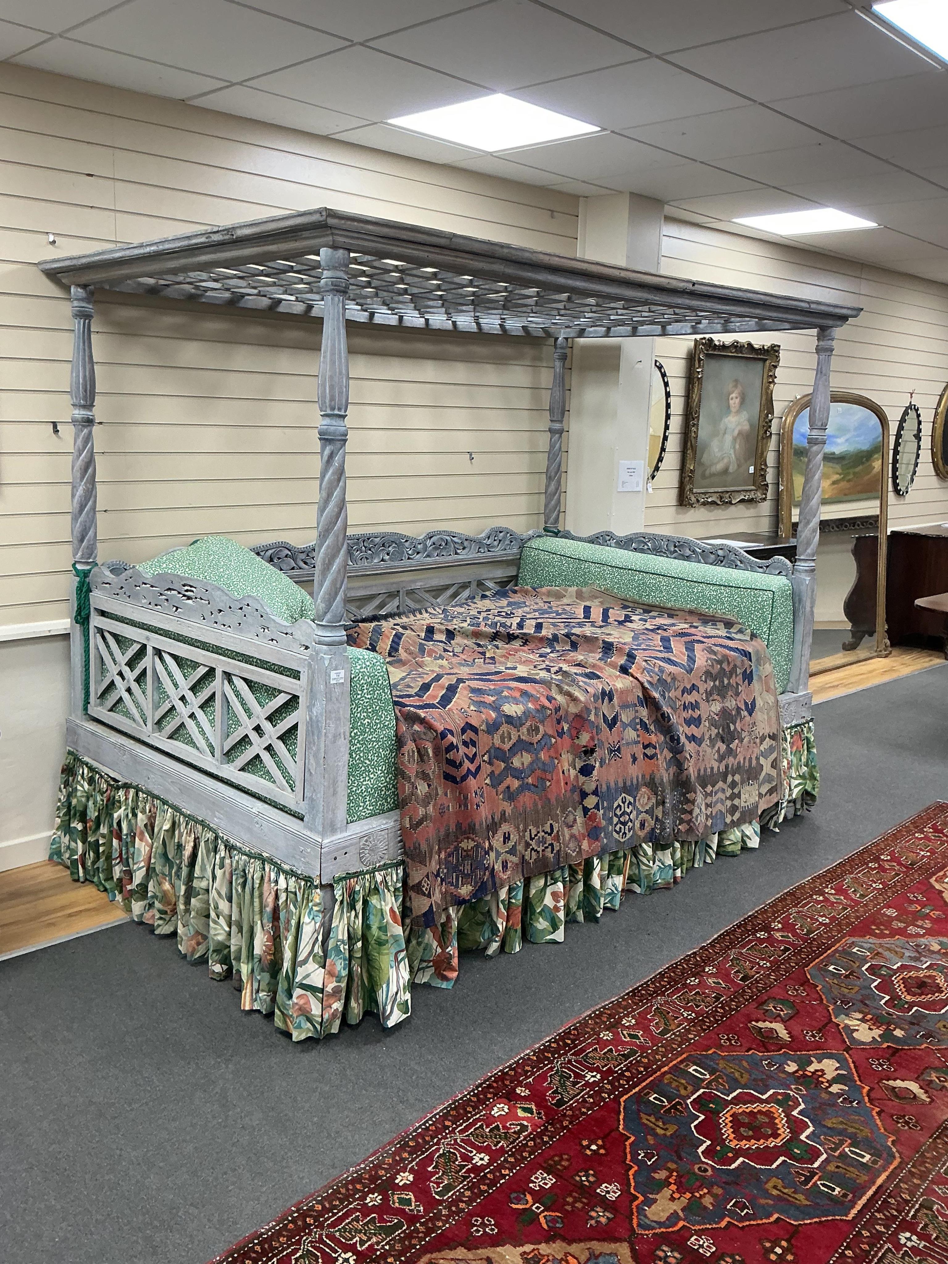 An Indian grey painted carved teak four poster double bedstead, with a pierced canopy over